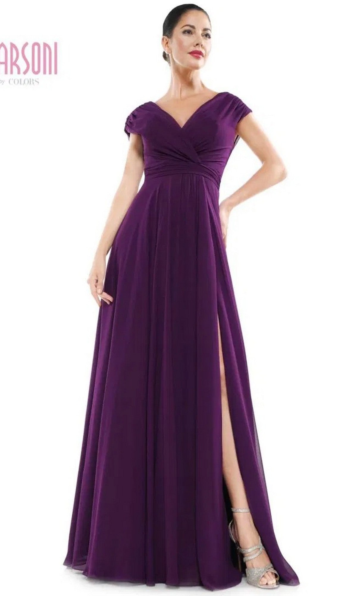 A woman stands with one hand on her hip, wearing the Marsoni M251 long formal dress in eggplant—a floor-length chiffon gown featuring cap sleeves, a v-neckline, and a high slit.